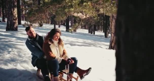 Молодая пара веселится катаясь на санках по заснеженным горным лесам — стоковое видео