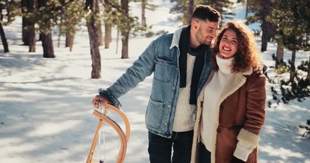 Молодая романтическая пара с санями, целующимися в снегу — стоковое видео