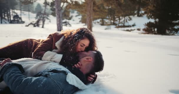 Jovem casal apaixonado deitado na neve e beijando — Vídeo de Stock