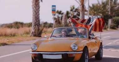 Amerikan bayrağı taşıyan kadınlar deniz kenarında üstü açık araba kullanıyorlar.