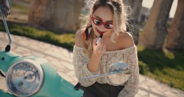 Mujer joven y elegante con scooter aplicando lápiz labial rojo en Italia — Vídeos de Stock