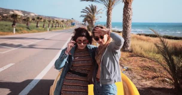 Mujeres de pie junto a un coche descapotable en la carretera de palmera junto al mar — Vídeo de stock