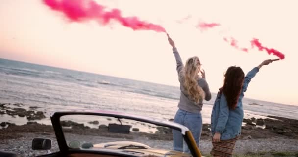 Amigos con coche descapotable celebrando con bombas de humo en la playa — Vídeo de stock