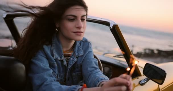 Frau im Cabrio hält Wunderkerzen am Strand bei Sonnenuntergang — Stockvideo