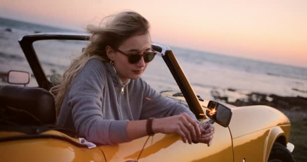 Γυναίκα χαλαρώνοντας σε μετατρέψιμο αυτοκίνητο και κρατώντας sparklers στο ηλιοβασίλεμα — Αρχείο Βίντεο