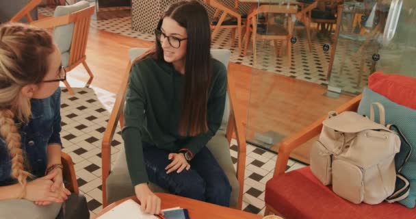 Unga tonårstjejer med surfplatta som studerar till skolan på caféet — Stockvideo