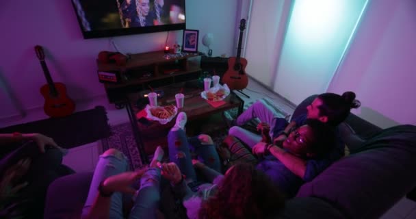 Genç çok ırklı oda arkadaşları kanepede dinleniyor ve birlikte televizyon izliyorlar. — Stok video