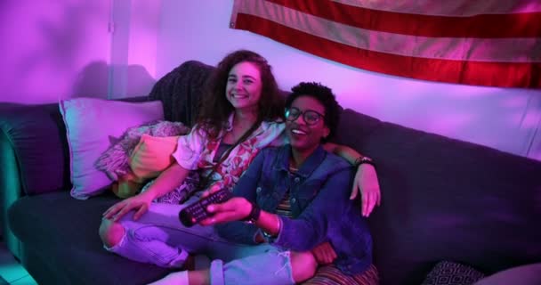 Щасливі багатоетнічні дівчата розважаються дивитися телевізор на дивані — стокове відео
