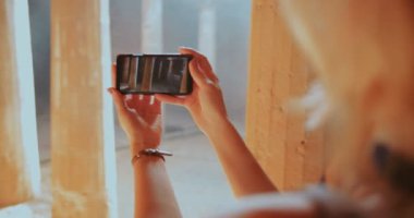 Akıllı telefonlu genç bir kadın antik taş sütunların fotoğraflarını çekiyor.