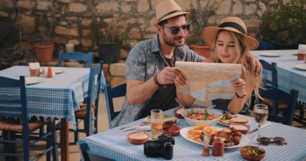 Jóvenes turistas pareja leyendo mapa en restaurante griego tradicional — Vídeos de Stock