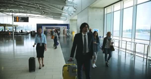 Мультиэтнические путешественники с чемоданами, идущие в международном аэропорту — стоковое видео