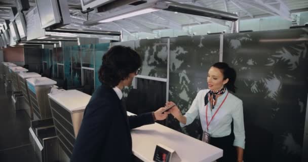 Joven hombre de negocios en el aeropuerto haciendo check-in en el mostrador de la aerolínea — Vídeo de stock