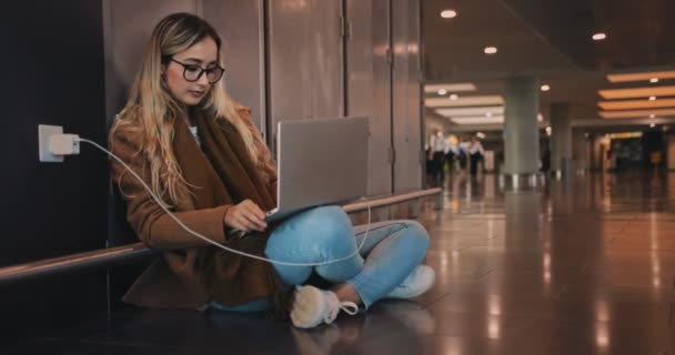 Молода жінка мандрівник заряджає ноутбук і працює в аеропорту — стокове відео