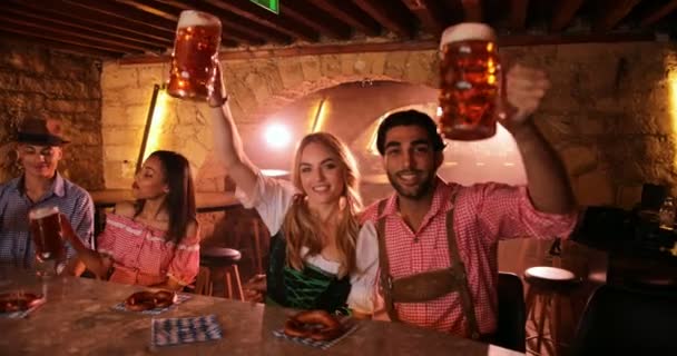 Νεαρό ζευγάρι γιορτάζει Oktoberfest με μπύρα και κουλούρια στο μπαρ — Αρχείο Βίντεο