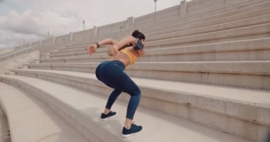 Genç atletik kadın spor yapıyor ve şehir stadyumunun merdivenlerinde atlıyor.