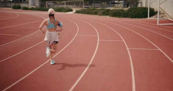Jeune coureuse faisant de l'entraînement sur piste et écoutant de la musique — Video