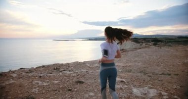 Gün batımında deniz yamacında koşan zinde bir kadın.