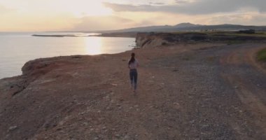 Aktif kadın gün batımında denizin üzerindeki uçurumda koşuyor.