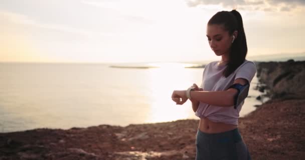 Mujer monitoreando su progreso de fitness en smartwatch al aire libre al atardecer — Vídeos de Stock