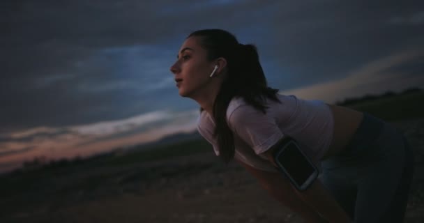 Женщина отдыхает и слушает музыку после тренировки на природе — стоковое видео