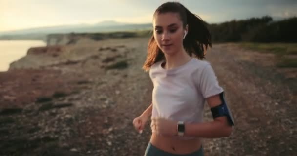 Corridore femminile che fa jogging sulla scogliera del mare e ascolta musica — Video Stock