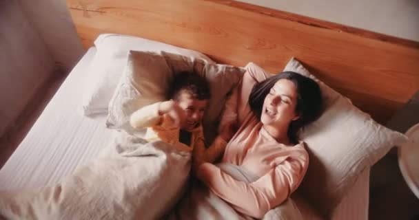 Мать и маленький сын обнимаются в постели утром — стоковое видео