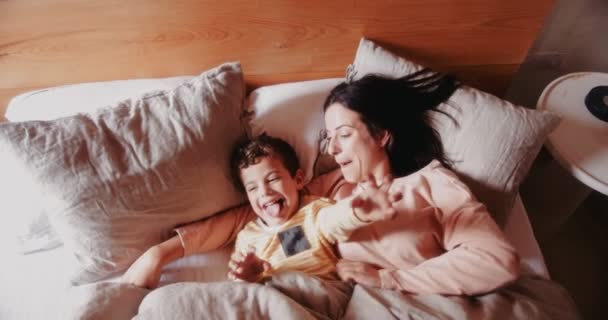 Νεαρή μητέρα και γιος χαλαρώνουν και διασκεδάζουν στο κρεβάτι — Αρχείο Βίντεο