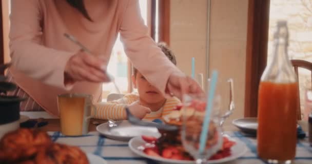 Mor serverar ung son sitter på bord pannkakor till frukost — Stockvideo