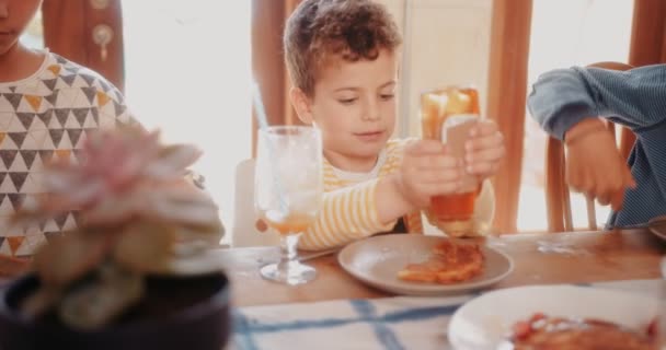 Giovane ragazzo che aggiunge miele sulla frittella durante la colazione con la famiglia — Video Stock