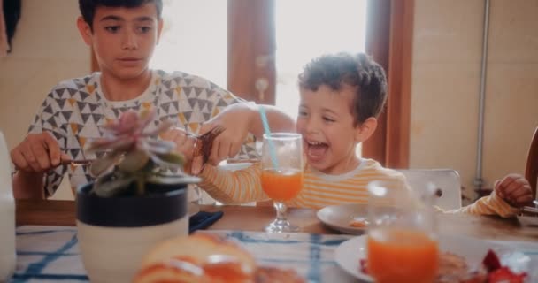 Oudere broer deelt pannenkoeken bij het ontbijt met jongere broer en zus — Stockvideo