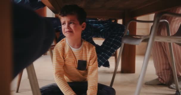 Sorglig gråtande pojke sitter under köksbordet under frukost — Stockvideo