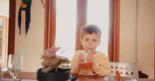 Jongen drinkt vers sinaasappelsap voor het ontbijt klaar is — Stockvideo