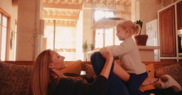Νεαρή μητέρα και κόρη διασκεδάζουν παίζοντας μαζί στον καναπέ — Αρχείο Βίντεο