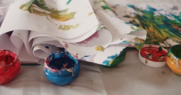 Открыть акриловые краски бутылки с детскими рисунками на грязном столе — стоковое видео