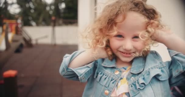 Mädchen mit blauen Augen und lockigem Haar auf Kindergartenspielplatz — Stockvideo