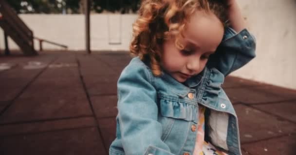 Onnellinen pieni tyttö, jolla on kiharat hiukset leikkipaikalla leikkiaikana — kuvapankkivideo