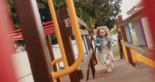 Chica con el pelo rizado corriendo en el jardín de infantes parque infantil selva gimnasio — Vídeo de stock