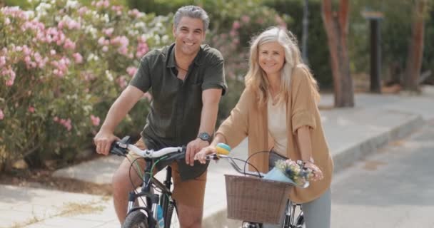Улыбающаяся взрослая пара, катающаяся на велосипедах в парке — стоковое видео