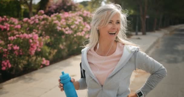 Mujer madura tomando un descanso de correr al aire libre y beber agua — Vídeo de stock