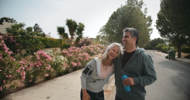 Feliz pareja mayor descansando y bebiendo agua después de hacer ejercicio de jogging — Vídeo de stock