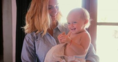 Genç anne kucağında küçük, tatlı, gülümseyen bir bebek tutuyor.