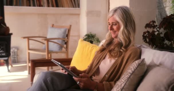 Μοντέρνα ώριμη γυναίκα που διασκεδάζει χρησιμοποιώντας tablet στο σπίτι — Αρχείο Βίντεο