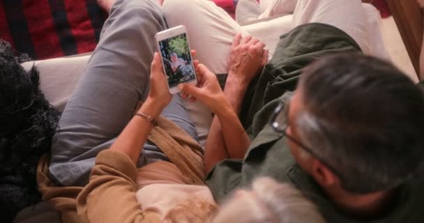 Старшая пара дома смотрит фотографии на смартфоне — стоковое видео