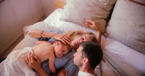 Любящие родители отдыхают в постели с маленьким сыном — стоковое видео