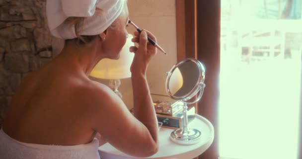 Volwassen vrouw toepassing make-up en kijken in spiegel thuis — Stockvideo