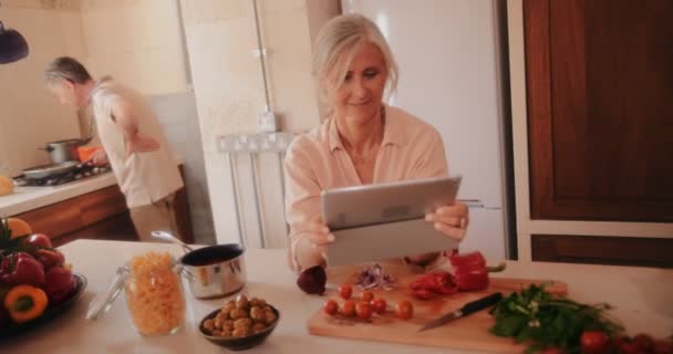 Senior par använder surfplatta och matlagning i köket hemma — Stockvideo