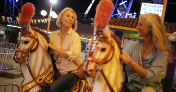 Mulheres maduras na moda se divertindo no parque de diversões passeio alegre-go-round — Vídeo de Stock