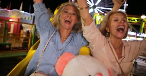 Mujeres maduras montando montaña rusa de feria de atracciones con los brazos extendidos — Vídeos de Stock