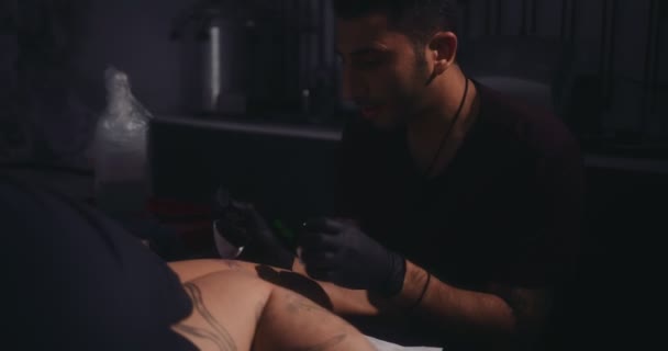 Молодий художник татуювання хіпстера робить татуювання на нозі чоловіка — стокове відео