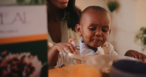 Joven madre alimentando a su pequeño hijo con cereales por la mañana — Vídeo de stock